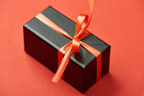 black gift box with bow and ribbon on red background - Valokuva, kuva