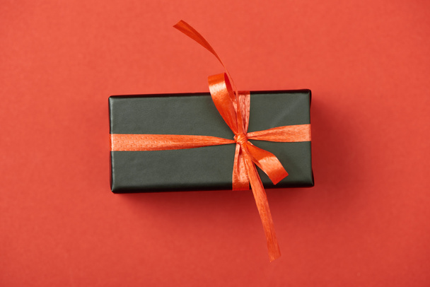 top view of black gift box with bow and ribbon on red background - Zdjęcie, obraz