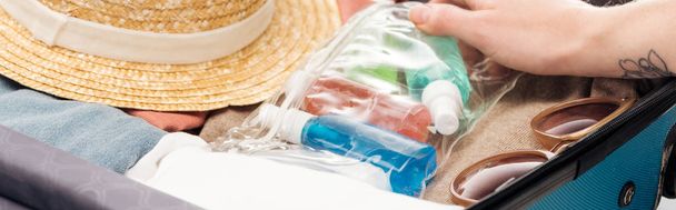 panoramisch schot van vrouw verpakking reistas met cosmetische tas met flessen - Foto, afbeelding