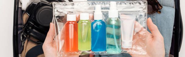 panoramisch schot van vrouw verpakking reistas met cosmetische tas met kleurrijke flessen - Foto, afbeelding