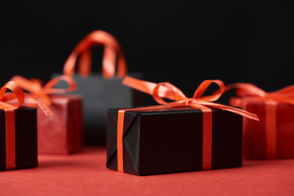 selective focus of presents with red ribbons and shopping bag isolated on black - Valokuva, kuva