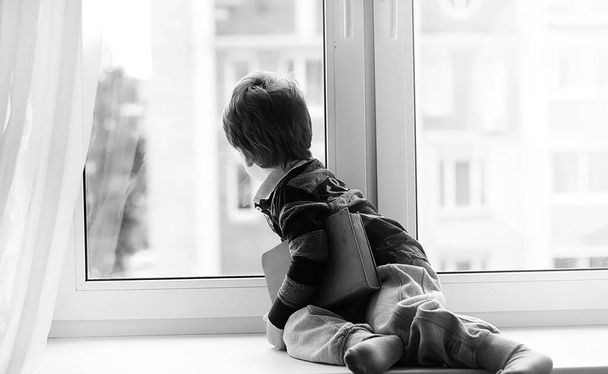 O rapazinho está a ler um livro. A criança senta-se na janela de um
 - Foto, Imagem
