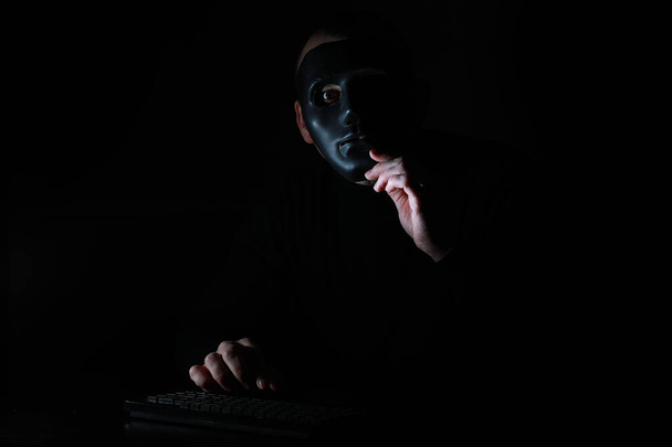 A man in a mask prints on the keyboard in the dark - Photo, Image