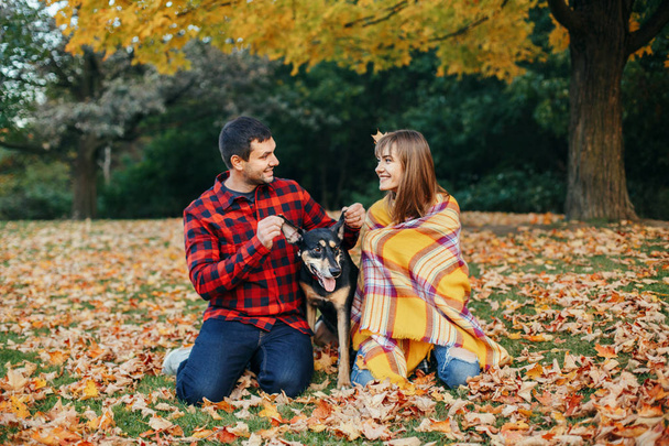 Beautiful young couple with dog in park. Man and woman hugging playing with their domestic animal pet outdoor on autumn fall day. Family authentic lifestyle activity. Love and friendship. - Photo, Image