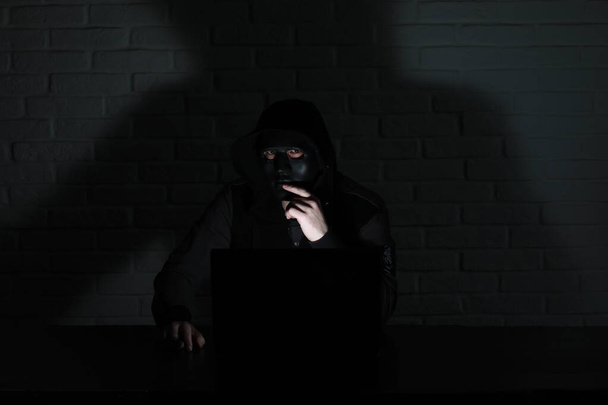 Хакер в черной маске и капюшоне за столом
 - Фото, изображение