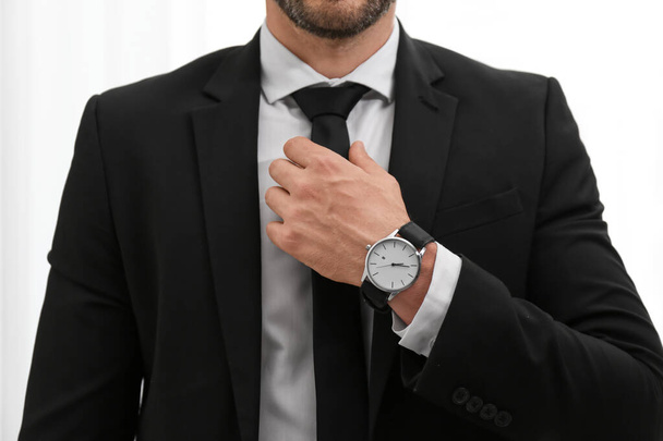 Businessman adjusting necktie on light background, closeup - Foto, afbeelding