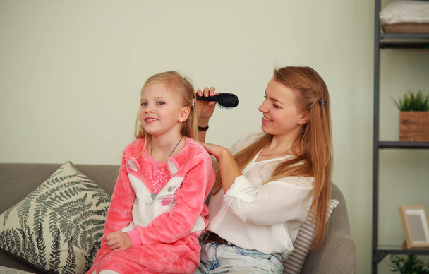 Mother caring for her daughter combing her hair at home - Foto, immagini