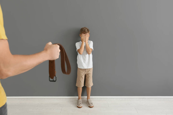Hombre amenazando a su pequeño hijo cerca de la pared gris. Concepto de castigo físico
 - Foto, imagen