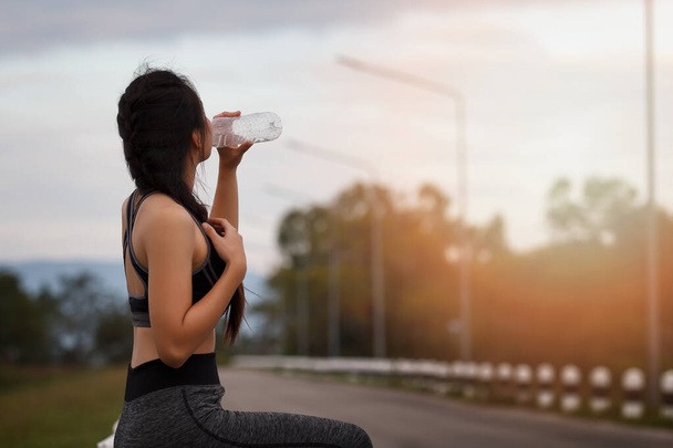 Atrakcyjna zdrowa dziewczyna fitness pijąca wodę po treningu. Biegaczka odpoczywa po treningu. - Zdjęcie, obraz