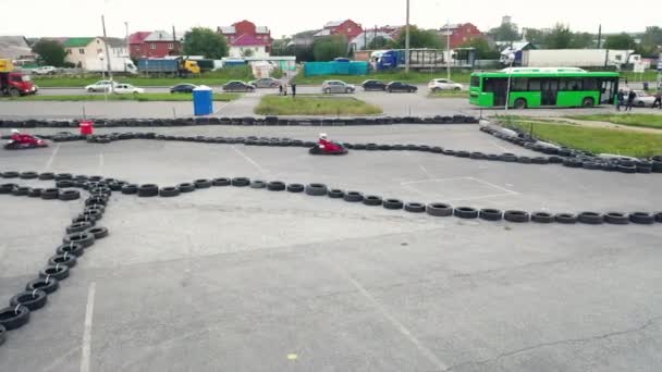 Kart racers in protective uniform and helmet moving on the track with old black car tires in the city in sunny day. Media. Karting Championship - Footage, Video