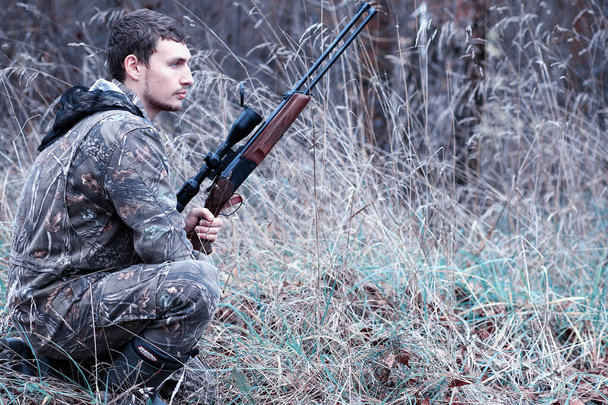 Um homem em camuflagem e com uma espingarda de caça em uma floresta em uma sp
 - Foto, Imagem