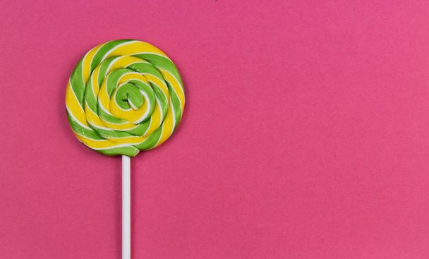 Yellow green spiral lollipop stock images. Colorful round lollipop on a pink background. Candy on a pink background with copy space for text - Photo, Image