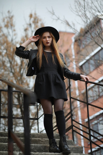 A girl walks down the city street in a leather waistcoat with a  - Фото, изображение