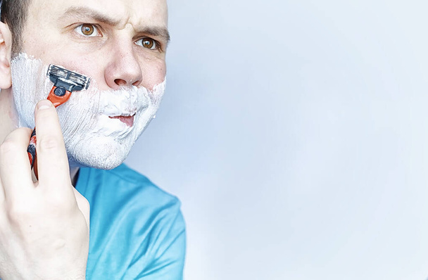 Un hombre se afeita delante de un espejo. Espuma de afeitar. Navaja desechable
. - Foto, imagen