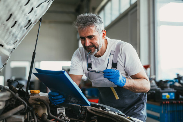 Mechaniker beim Blick auf Teilebroschüre im Autoservice - Foto, Bild
