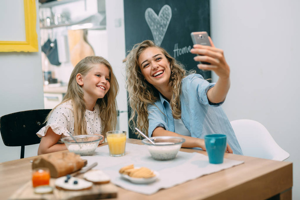Family having breakfast, mother and daughter taking selfie at home. - Photo, image