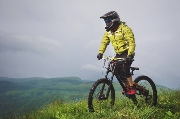 Front view of a man on a mountain bike standing on a rocky terrain and looking down against a gray sky. The concept of a mountain bike and mtb downhill - Foto, immagini