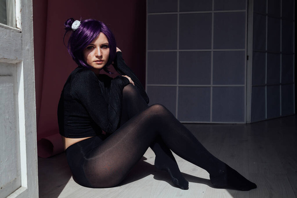 Tyttö violetti tukka istuu lattialla mustissa vaatteissa
 - Valokuva, kuva