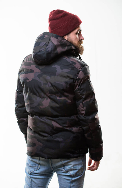 Hipster winter fashion. Guy wear hat and black winter jacket. Comfortable winter outfit. Winter stylish menswear. Man stand warm camouflage pattern jacket parka with hood isolated on white background - Fotó, kép