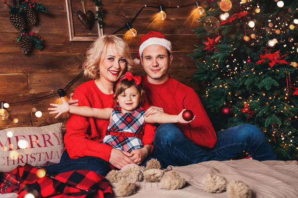 Noel ailesi ve Noel ağacının yanında gülümseyen bir çocuk. Noel ağacı ve hediye kutularıyla dekore edilmiş oturma odası. Işık rahat bir ortam sağlıyor. Yeni yıl tatili - Fotoğraf, Görsel