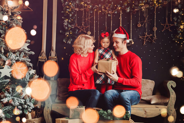 З Різдвом і з Новим Роком! Сім'я дарує коробку для дитини у вітальні, прикрашеній христмою - деревом і коробками з подарунками xmas. Портретна любляча сім "я. - Фото, зображення