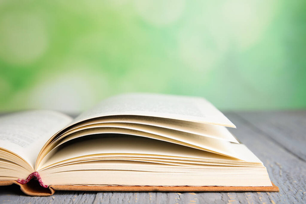 Открытая книга на сером деревянном столе на размытом зеленом фоне, крупным планом. Пространство для текста
 - Фото, изображение