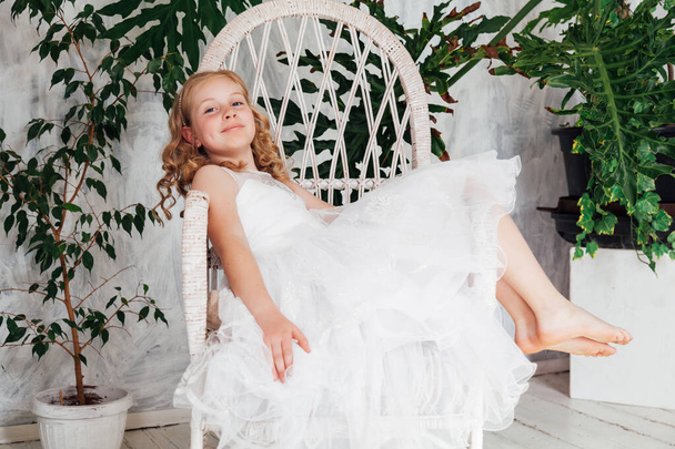 Hermosa chica rubia en vestido blanco se sienta en una silla
 - Foto, imagen