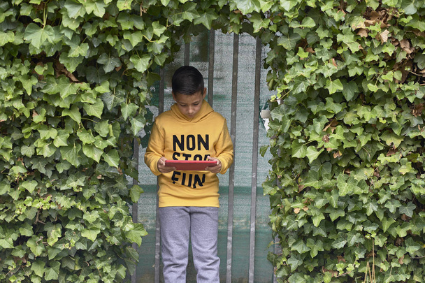 Junge mit grünen Augen surft mit verstecktem Tablet auf der Straße im Internet - Foto, Bild