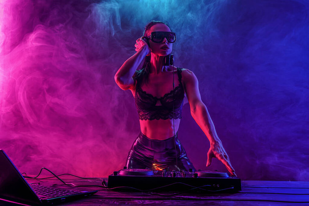 Young sexy woman dj playing music. Headphones and dj mixer on table. - 写真・画像