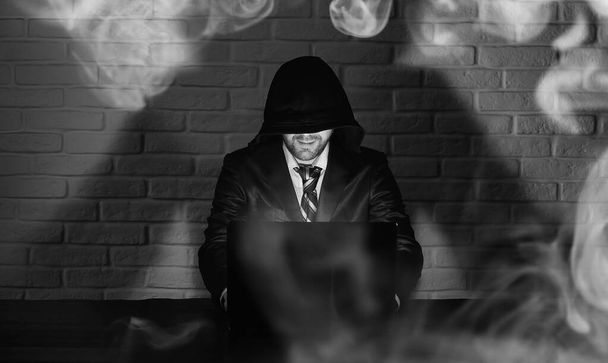 Χάκερ σε μαύρη μάσκα και καπό στο τραπέζι - Φωτογραφία, εικόνα