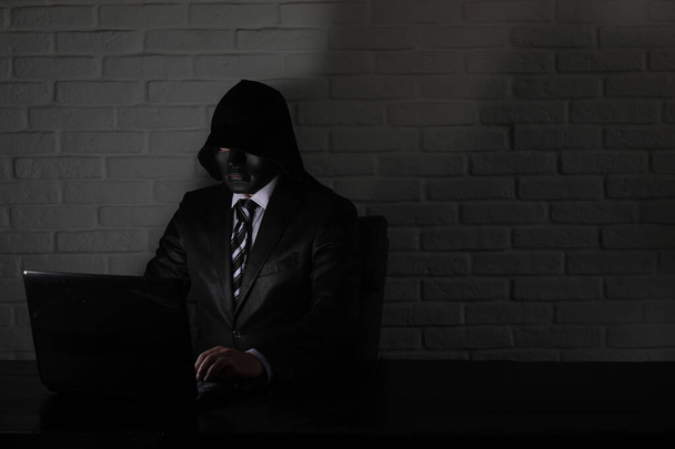 Hacker in zwart masker en capuchon aan de tafel - Foto, afbeelding