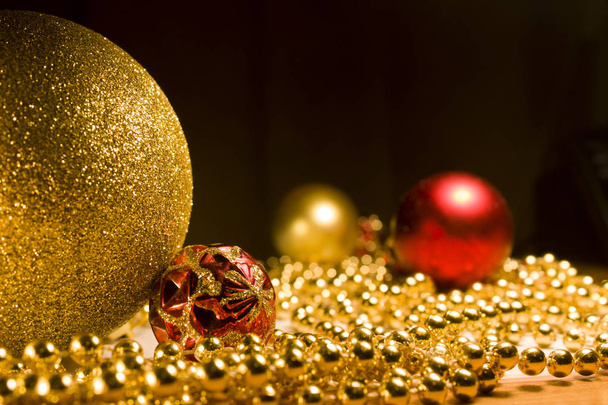 Christmas toys gold and red with gold beads on the table. Red ball with gold pattern. New year's footage with the Christmas tree decorations in warm colors - Foto, imagen