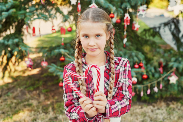 enfant fille avec des nattes et des bonbons à la séance photo de Noël "Noël en Juillet" sur le fond d'un arbre de Noël avec des cadeaux
 - Photo, image