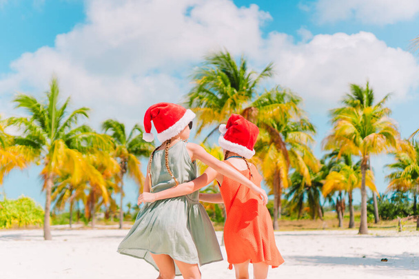 kleine entzückende Mädchen in Weihnachtsmützen während des Weihnachtsurlaubs am Strand, die zusammen Spaß haben - Foto, Bild