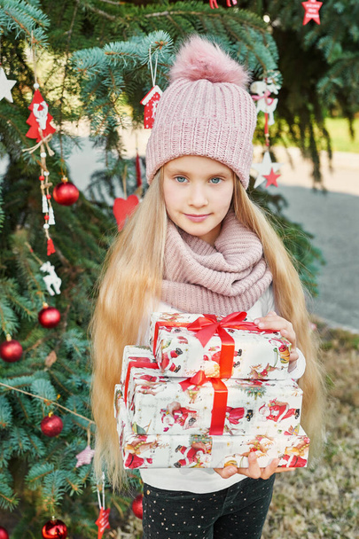 7月のクリスマスツリーの近くの帽子とスカーフの子供の女の子 - 写真・画像
