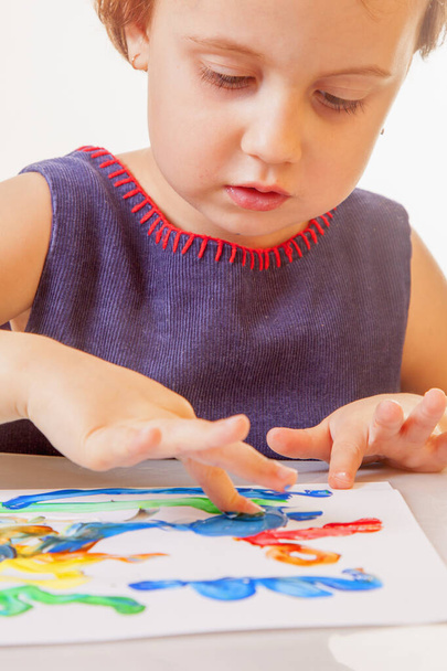 Маленька мила дівчинка малює різнокольоровими руками і пальцем
.  - Фото, зображення