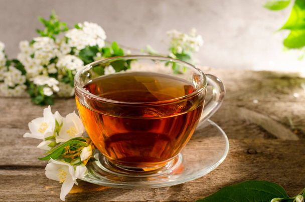 Gustoso tè profumato con fiore di gelsomino. Tazza da tè in vetro su un vecchio tavolo di legno. Bevanda calda con fiori di Filadelfo
. - Foto, immagini
