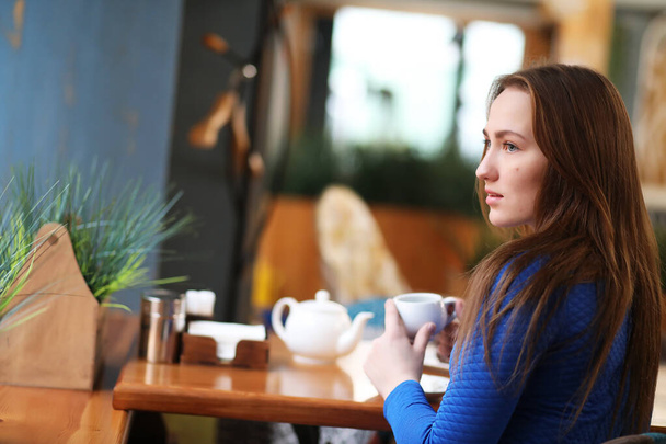 Молода дівчина в кафе сидить і п'є чай
 - Фото, зображення