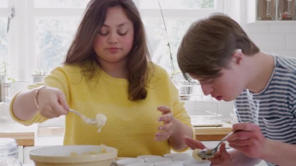 Young Downs Syndrome couple baking in kitchen at home putting mixture into cupcake cases - shot in slow motion - Footage, Video
