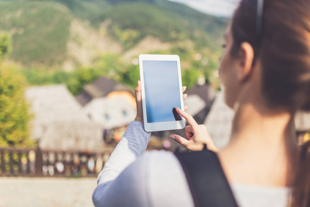 Female tourist holding blank screen digital tablet device against beautiful mountain village. Travel and technology concept. - Φωτογραφία, εικόνα