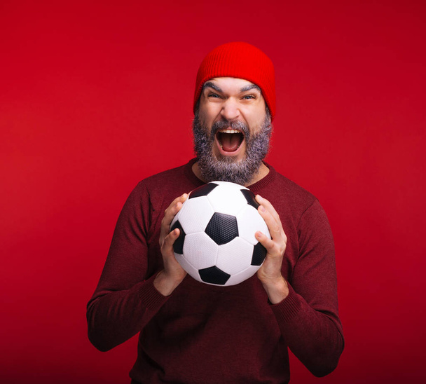 Возбужденный молодой человек с белой бородой кричит и держит футбольный мяч
 - Фото, изображение