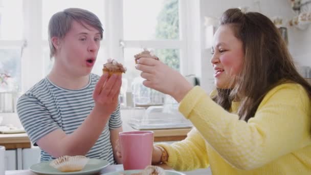 Jovens Downs Síndrome casal sentado em torno da mesa com bebida quente e bolos em casa falando - filmado em câmera lenta
 - Filmagem, Vídeo