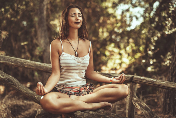 Beautiful young woman is doing yoga and meditating in the pine forest in summer. - Photo, image