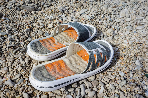 Zapomenuté plážové pantofle leží na oblázkech u moře - Fotografie, Obrázek
