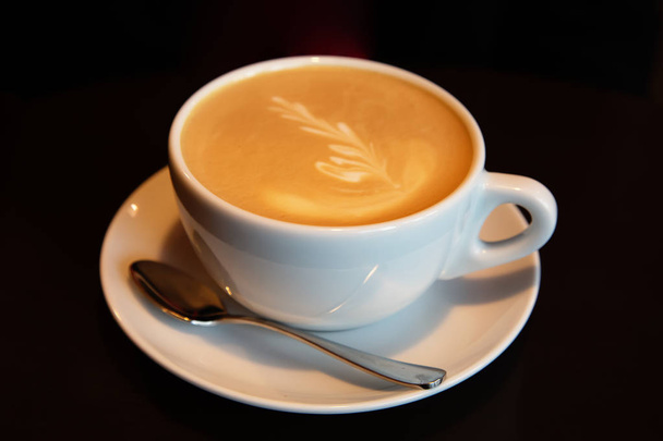 Ένα φλιτζάνι καφέ με αφρό στη σκοτεινή πλάτη - Φωτογραφία, εικόνα