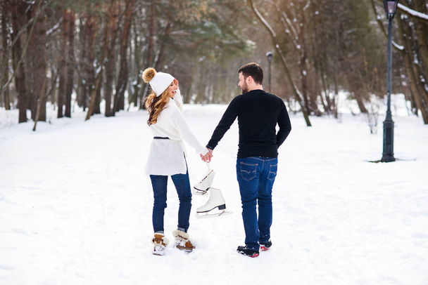 Close up loving couple walking on a date in a winter Park. Young man and his girlfriend holds each other to the hands and holding ice skates. - Foto, Imagen