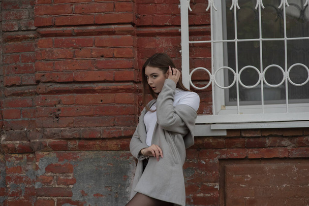 Gri paltolu genç kız bir şehir sokağının arka planında duruyor. Gri arka planda gri ceketli kız.. - Fotoğraf, Görsel