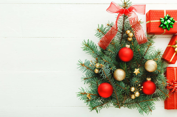 Kerst Nieuwjaar patroon samenstelling: Kerstboom gemaakt van sparren takken, rode geschenkdozen op witte houten achtergrond, concept van vakantie viering 2020. Vlakke lay, bovenaanzicht, kopieerruimte. - Foto, afbeelding