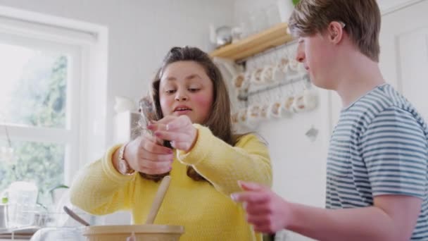 Young Downs Syndrome couple baking in kitchen at home decorating cupcakes with icing - shot in slow motion - Séquence, vidéo