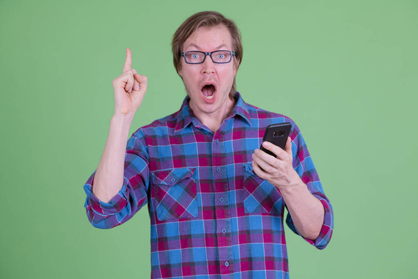 Shocked joven hipster hombre sosteniendo el teléfono y apuntando hacia arriba
 - Foto, imagen